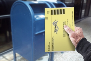 Person holding ballot in front of USPS mailbox