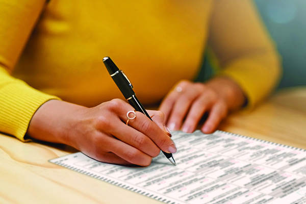 Closeup shot of an unrecognizable woman filling in paperwork on a clipboard at a table