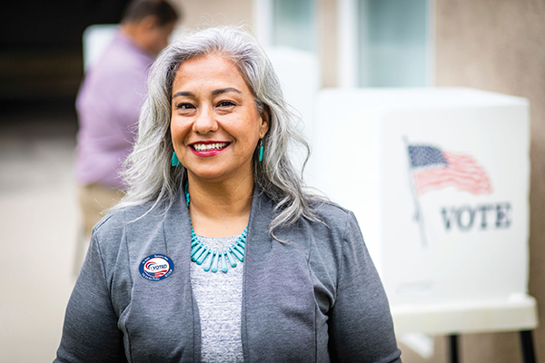 Woman wearing an 'I Voted Sticker' standing next to a voting booth